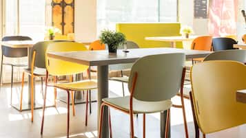 Un comedor moderno con mesas y sillas, ventanas amplias y una puerta visible con detalles metálicos.