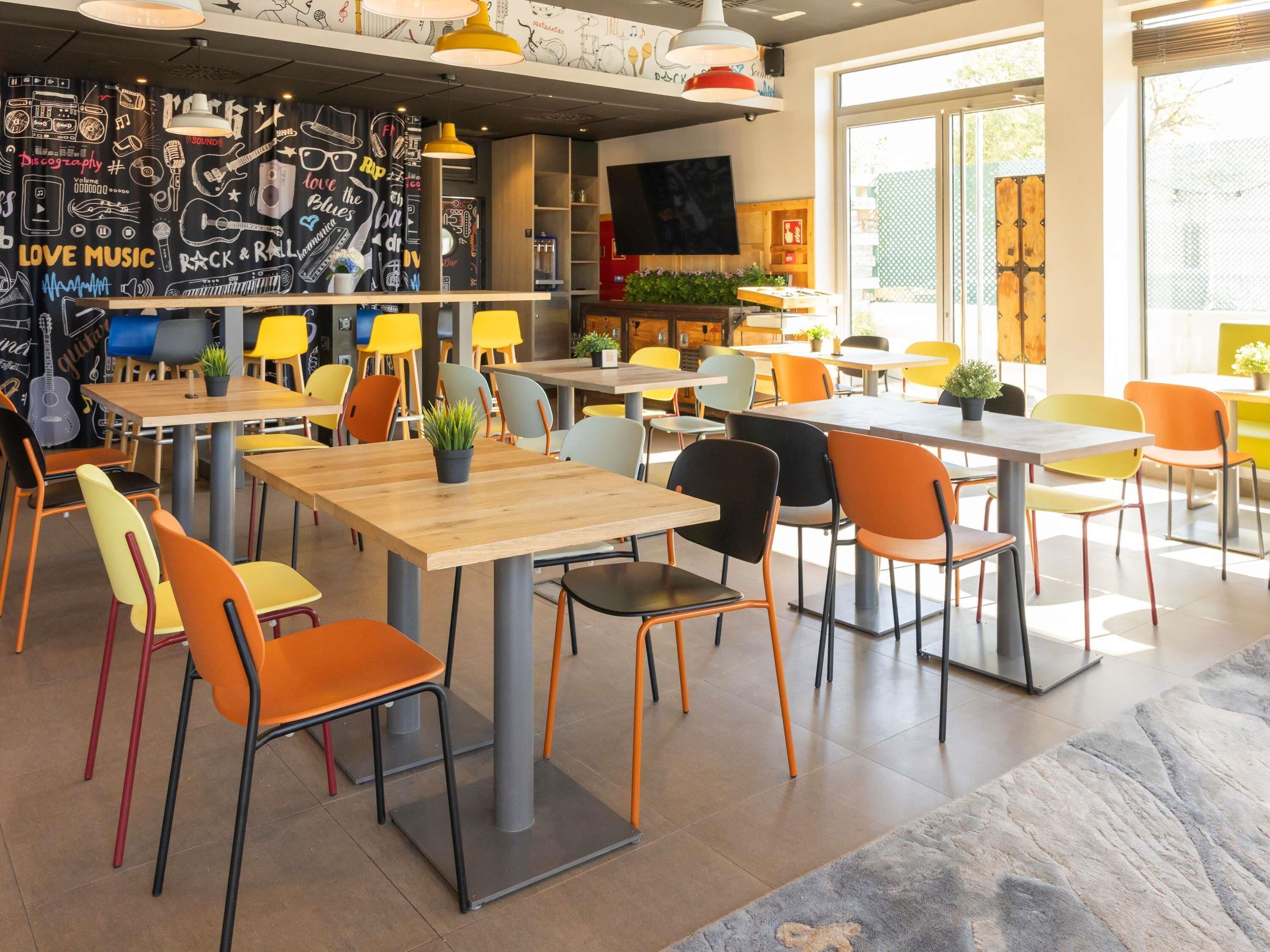 A modern cafe with colorful chairs and tables, a wall decorated with musical instruments and instruments, and a large window providing natural light.