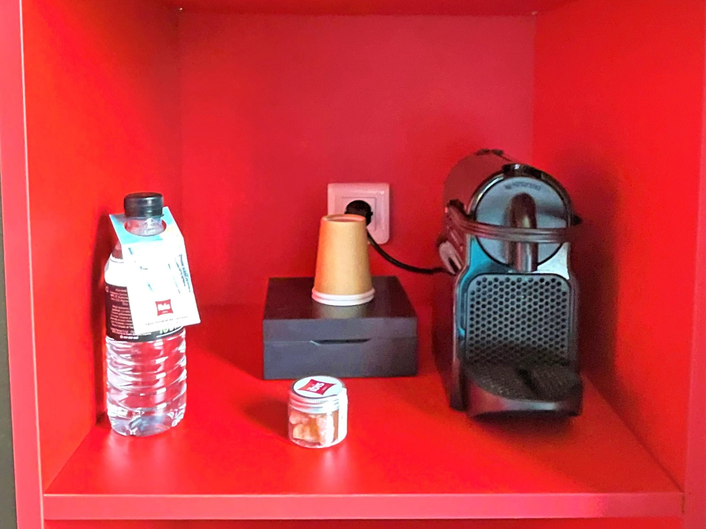 Ein rotes Regal mit einer Wasserflasche, einem kleinen Glas und einem tragbaren Lautsprecher.