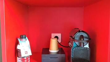 Una estantería roja con una botella de agua, un frasco pequeño y un altavoz portátil.