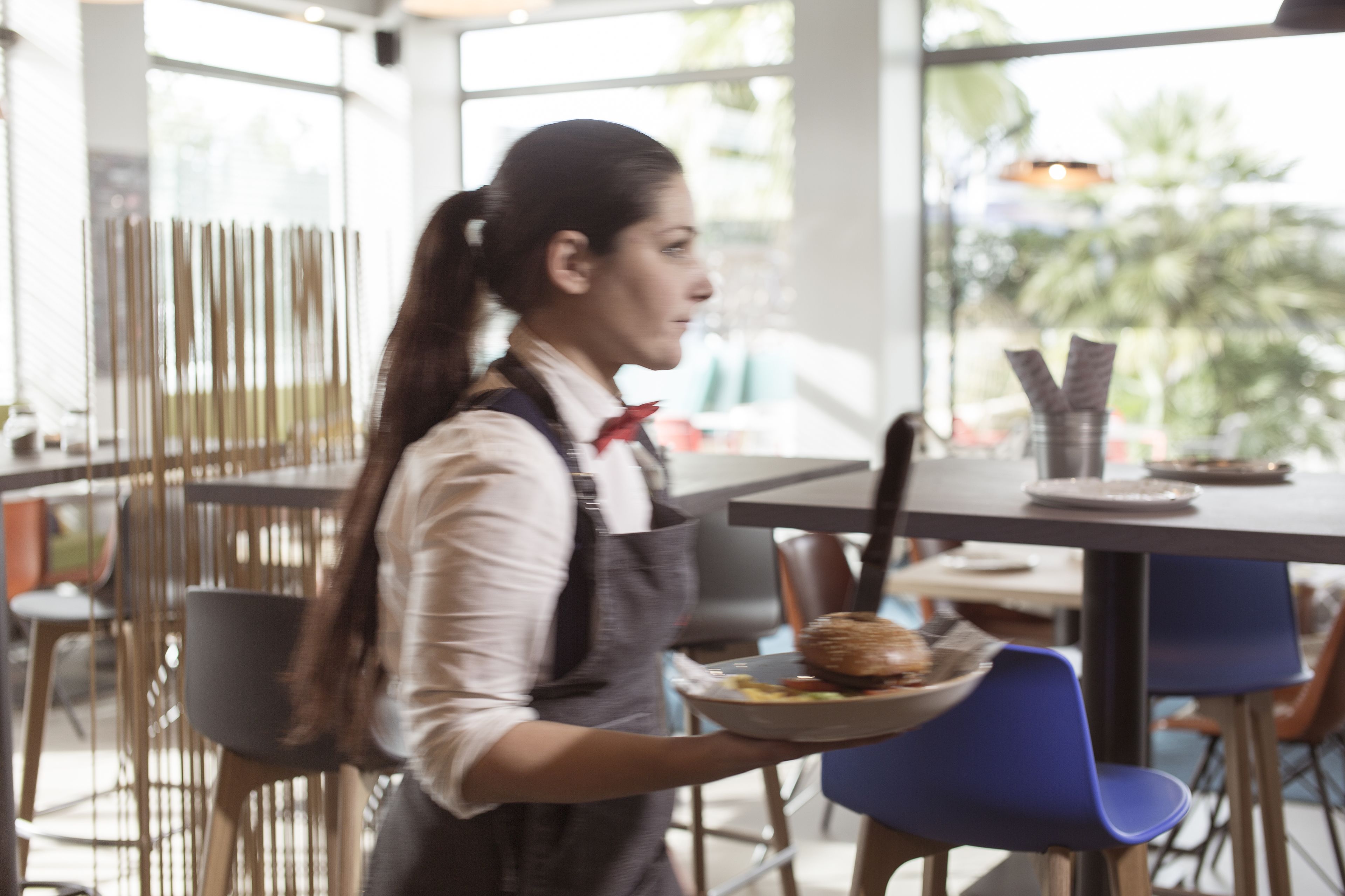 Una persona sirve comida en una cafetería moderna con un amplio ventanal y mobiliario contemporáneo.