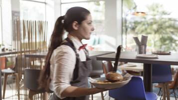 Una persona sirve comida en una cafetería moderna con un amplio ventanal y mobiliario contemporáneo.