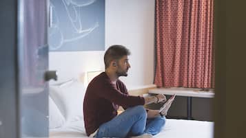 A person sitting on a bed in a hotel room, holding a tablet.