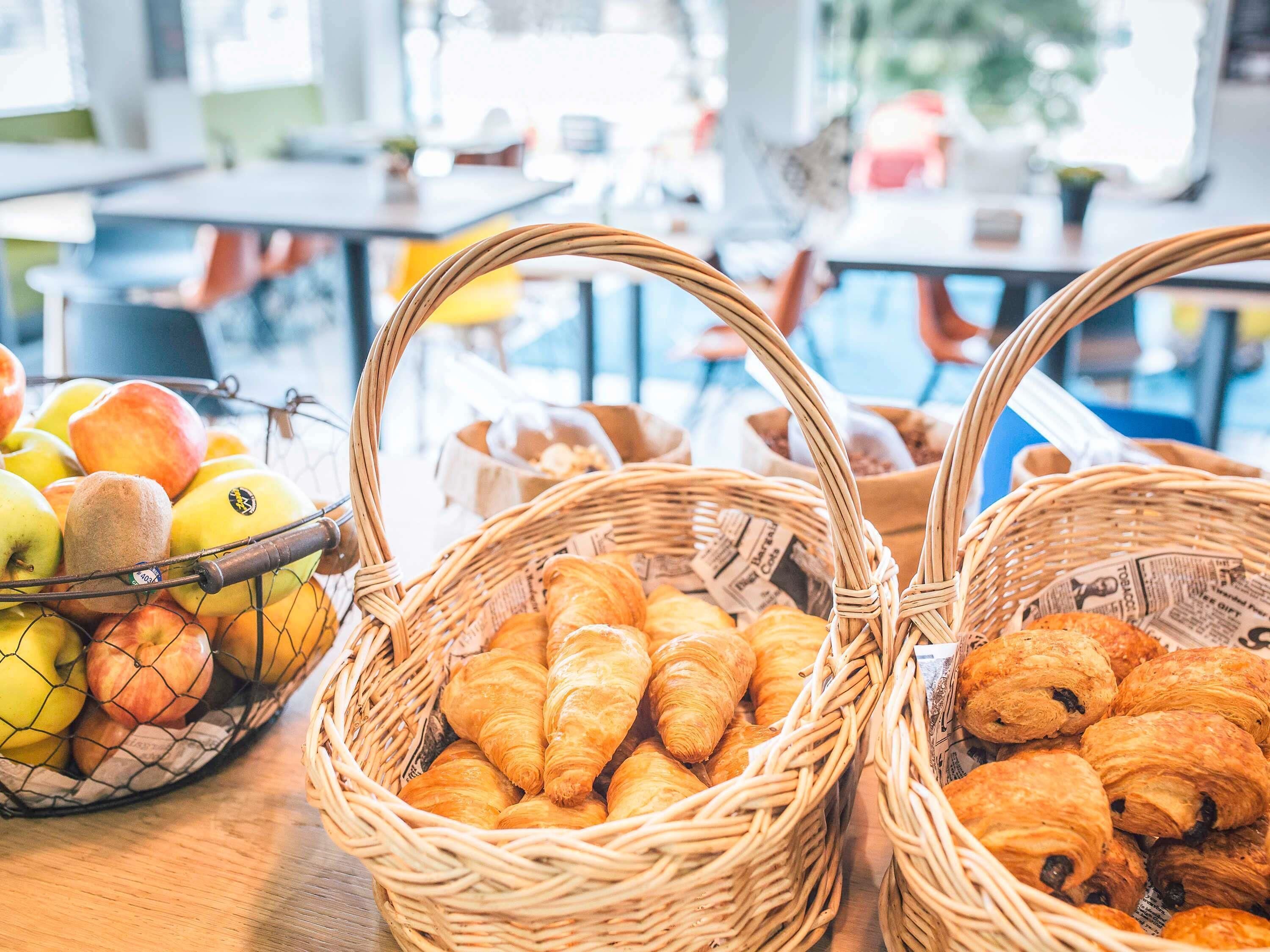 A breakfast buffet with baskets of fruits and pastries.