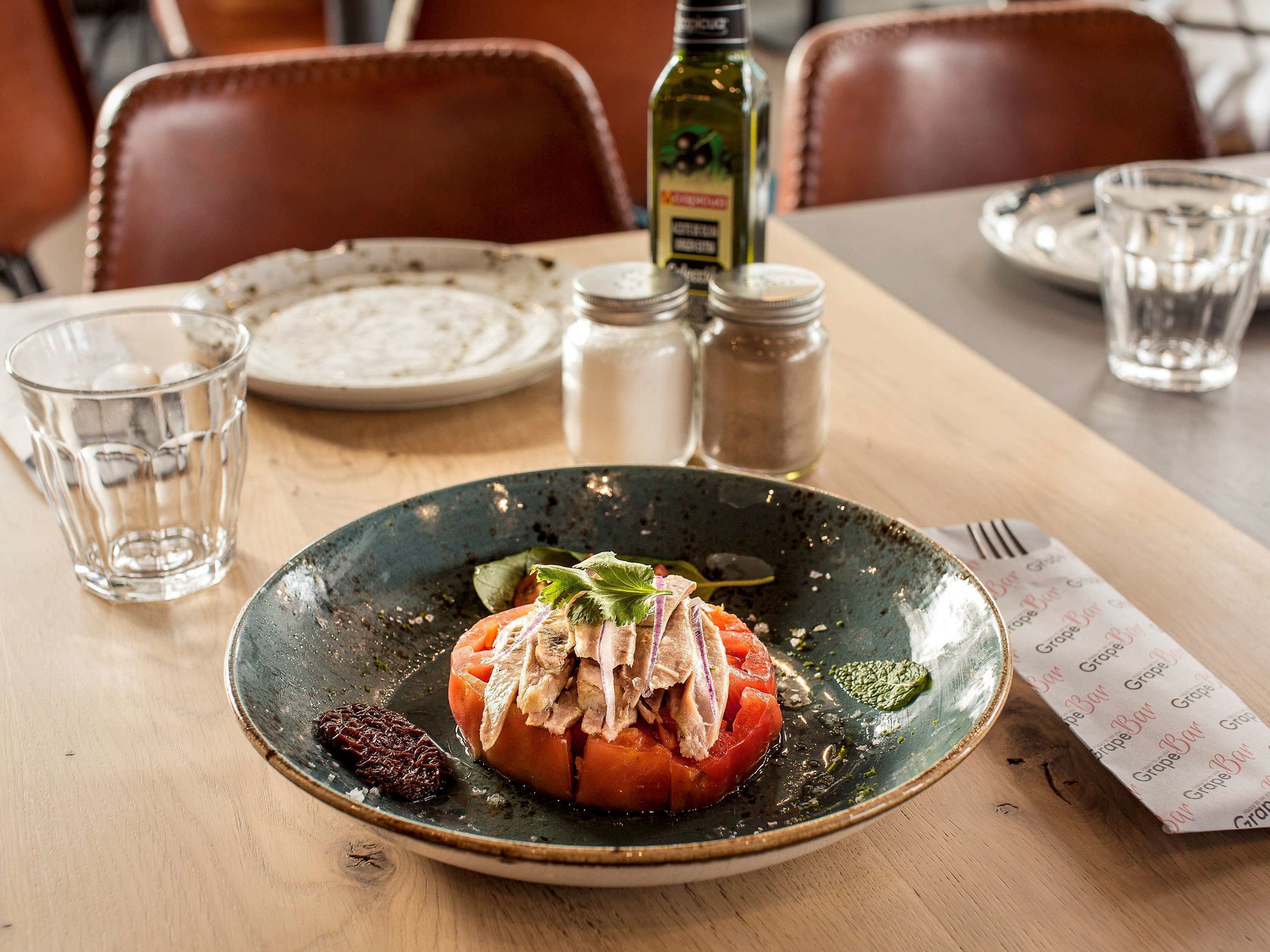 Une table à manger avec une assiette de nourriture, des salières et des poivrières, une bouteille et un menu.