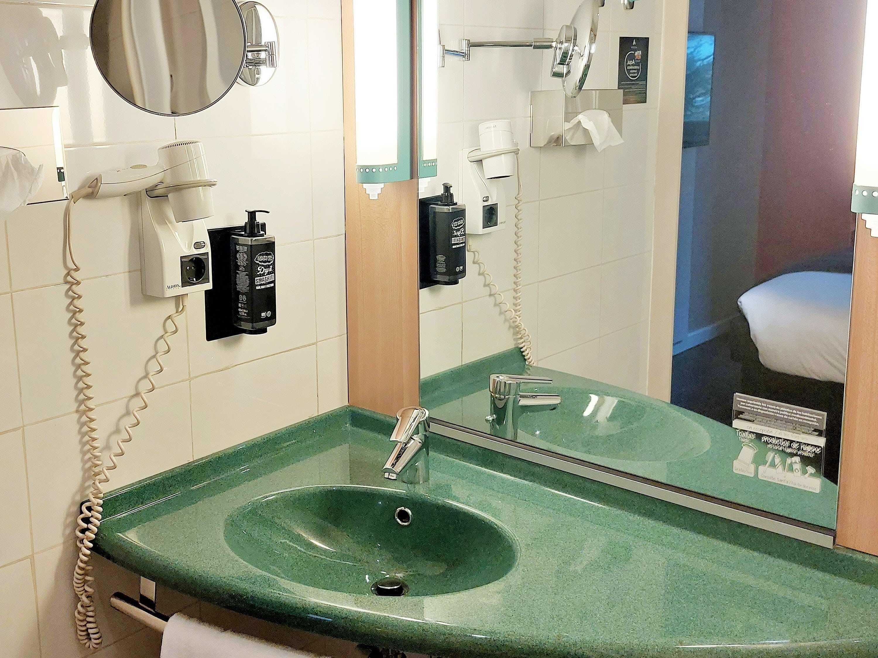 A bathroom with a green sink, a mirror, a hairdryer, and a towel rack.