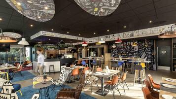 Een modern restaurant met een bar, verschillende zithoeken zoals tafels en stoelen, en een plafond met hangende lampen.