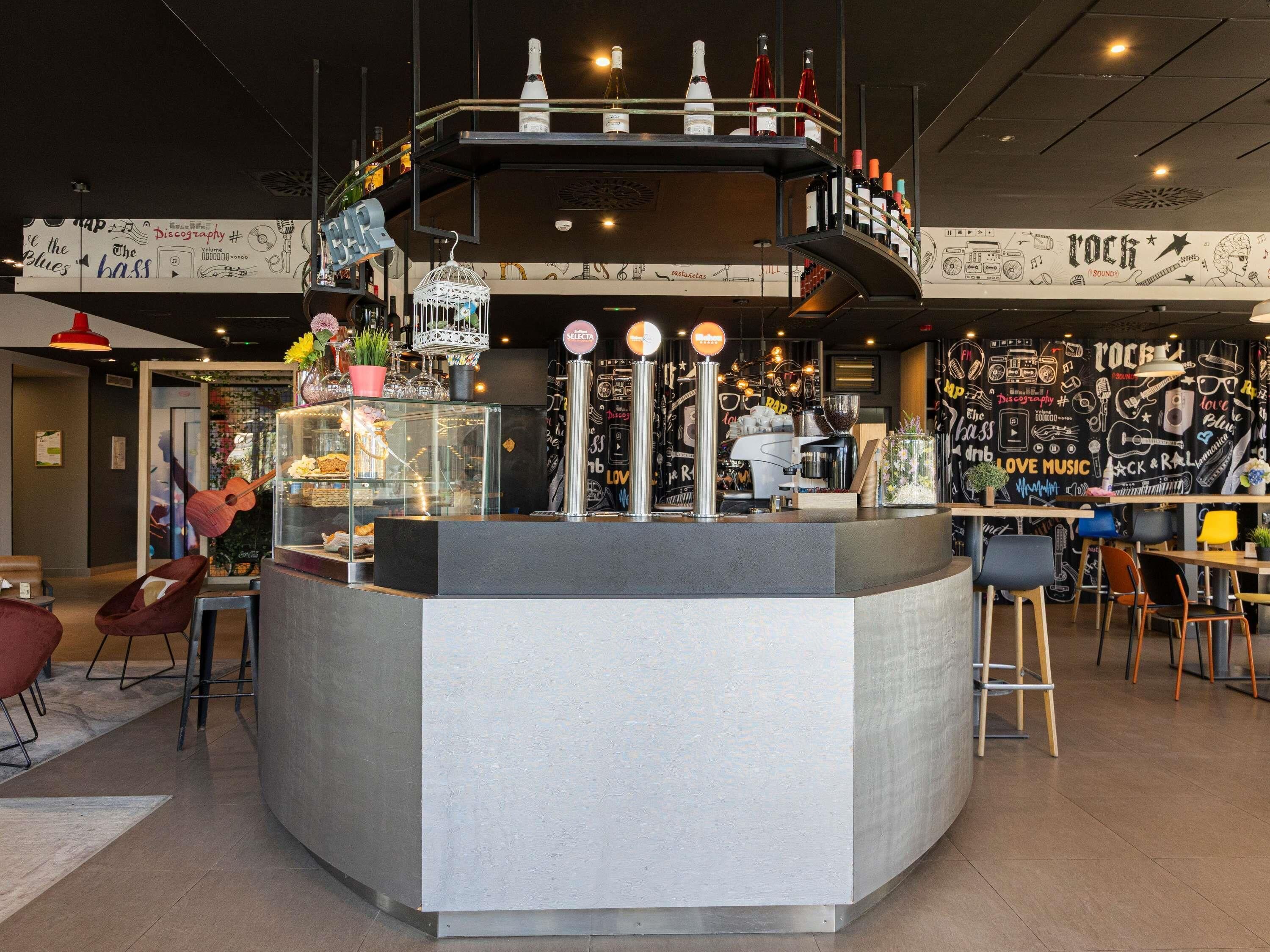 A bar area with a counter, stools, and a wall decorated with musical and cultural graphics.