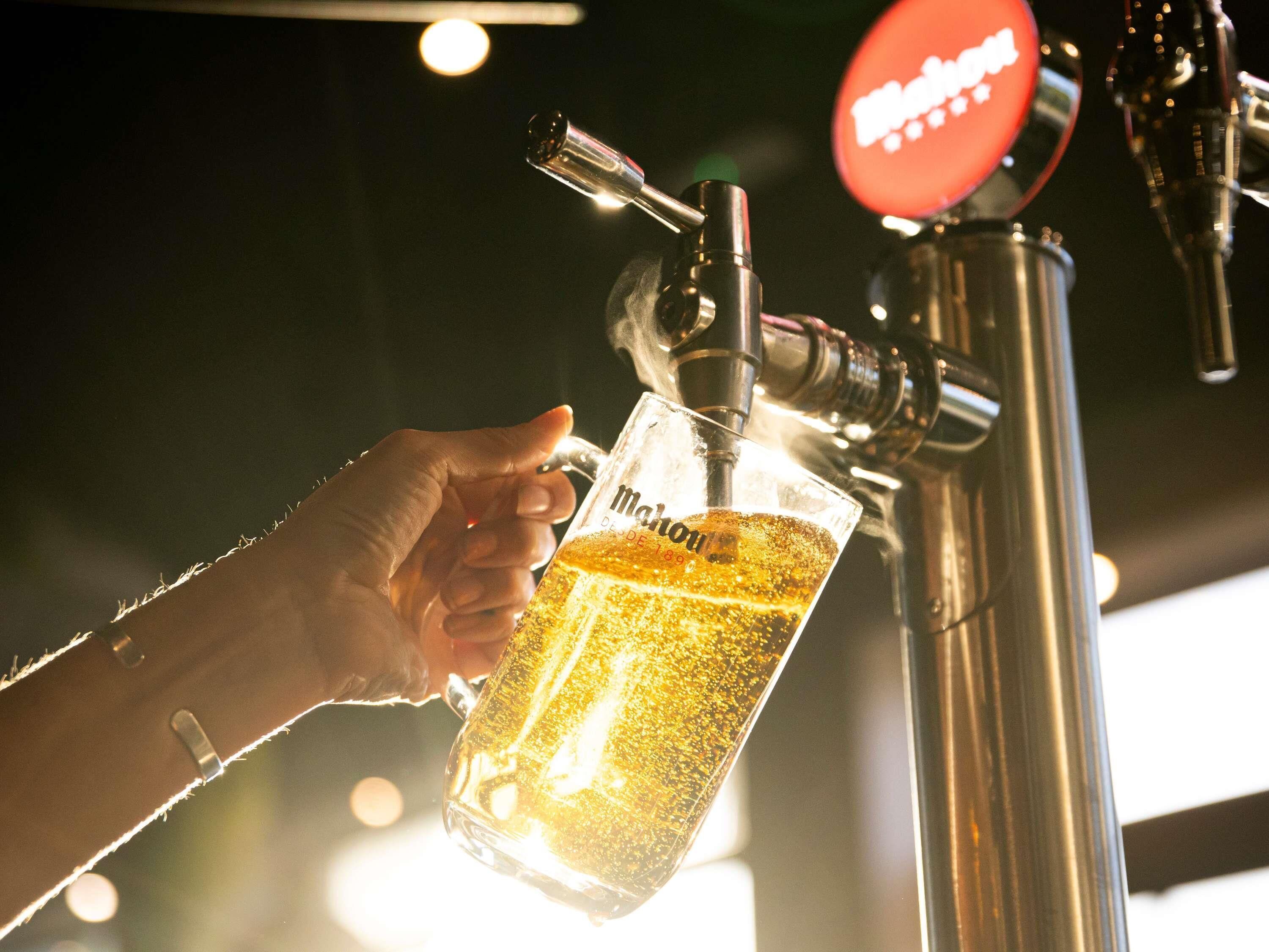 A hand holding a glass mug under a beer tap.
