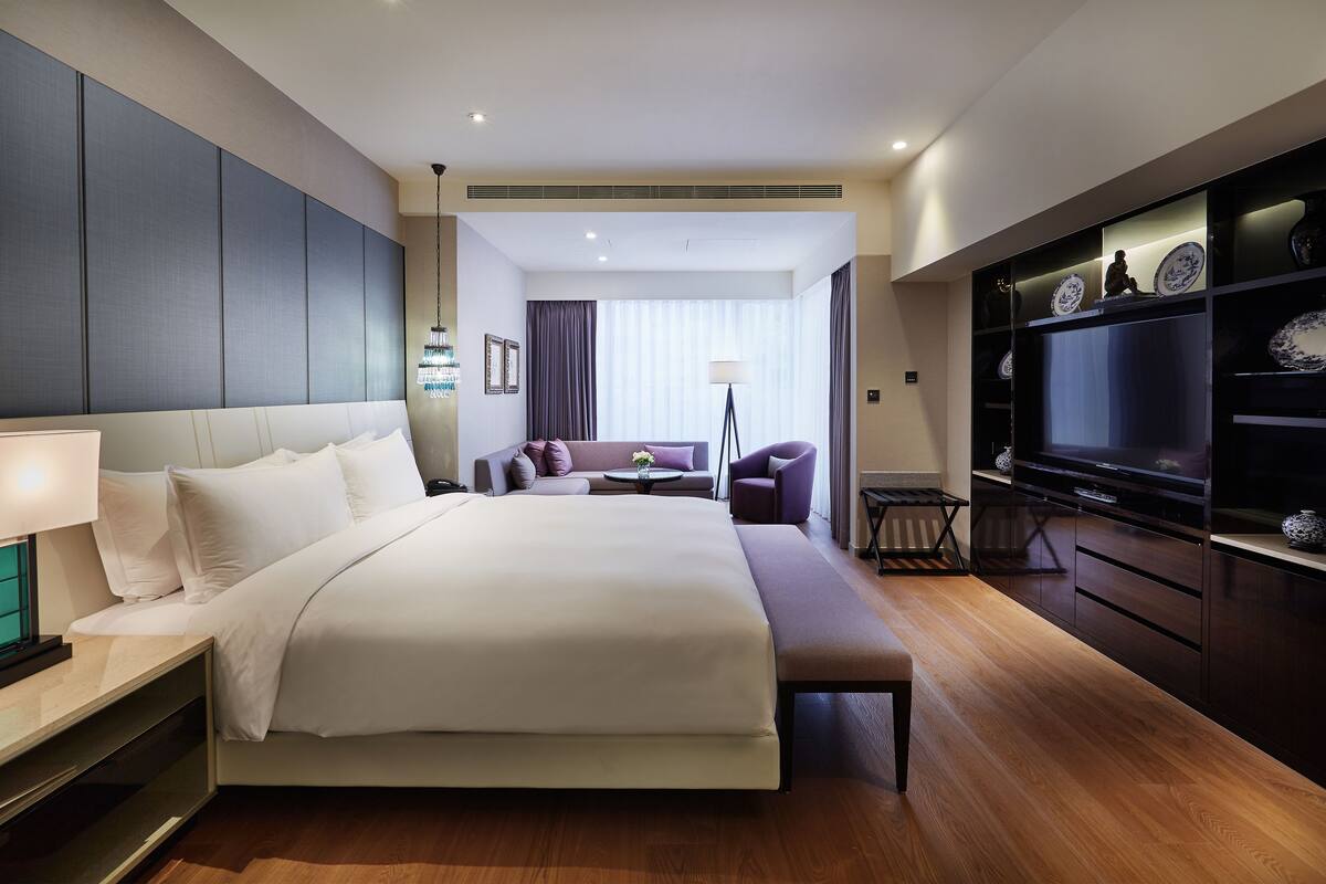 A modern hotel room with a large bed, a seating area with a sofa and armchairs, a television, and a minibar.