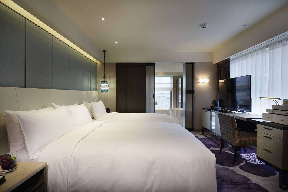 A hotel room with a large bed, a desk with a computer, a TV, and a window with curtains.