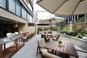 An outdoor patio area with wooden tables and chairs, large umbrellas, and potted plants. - Taipei Fullerton Hotel – Maison North (Taipei)