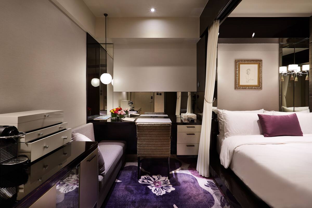 A modern hotel room with a bed, a desk, a vanity, and a large mirror.