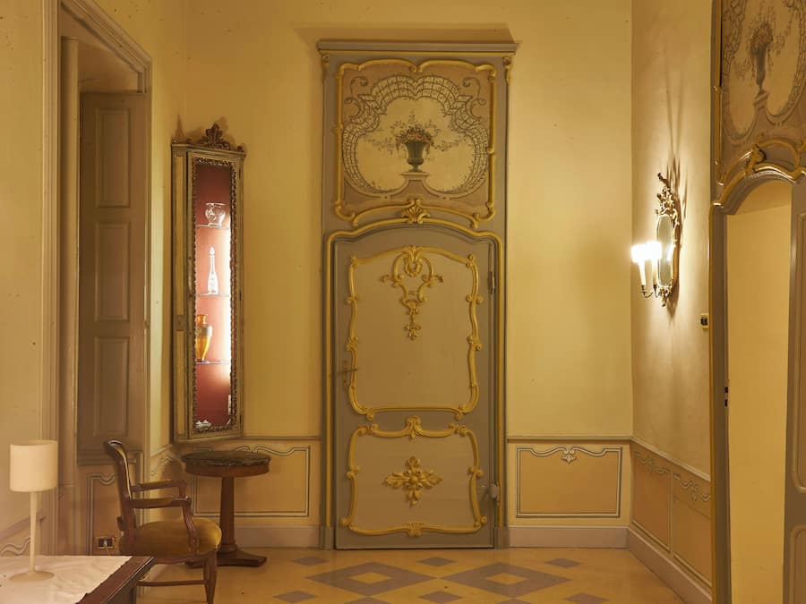 A room with a large ornate door, a mirror, a small table, and a chair.