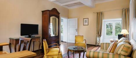 Una habitación con televisión, muebles de madera, una alfombra estampada y una ventana con cortinas.
