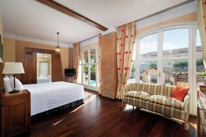 Habitación de hotel con cama, sofá, televisión y ventanas amplias que ofrecen vistas al exterior.