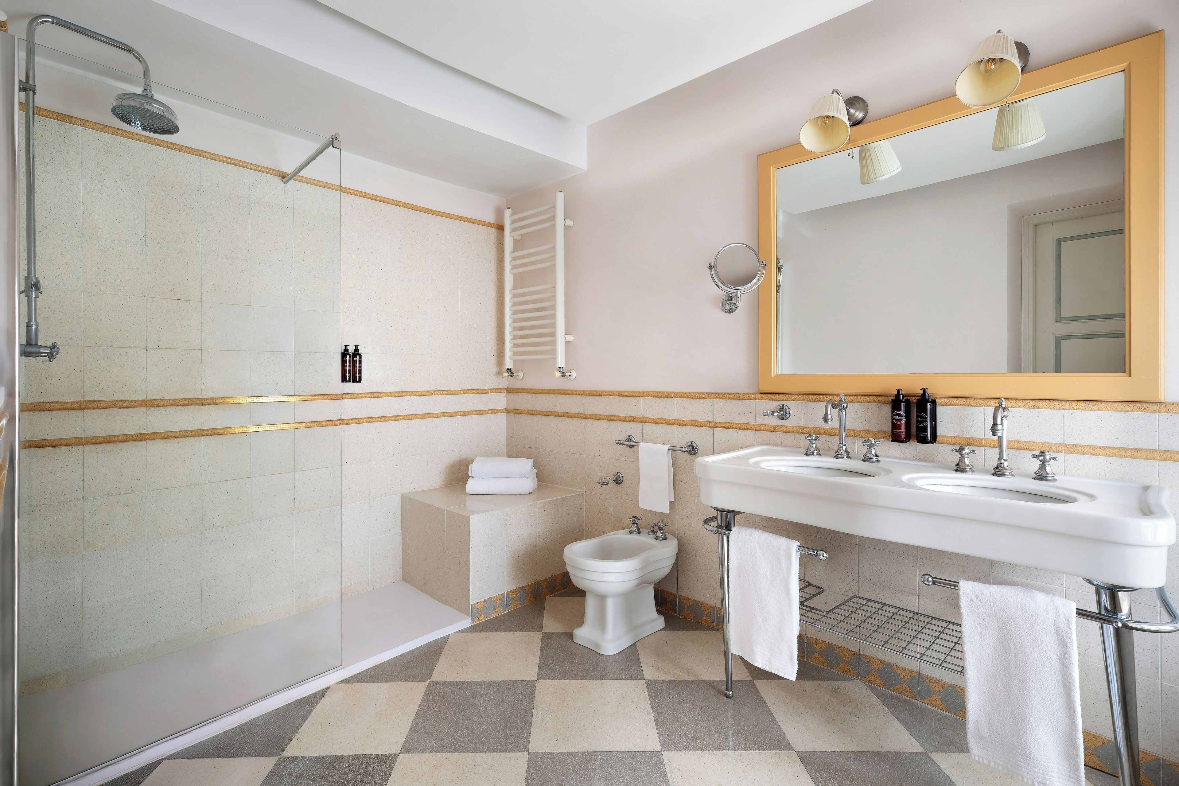 Un baño con ducha, bidé, dos lavamanos y un espejo grande.
