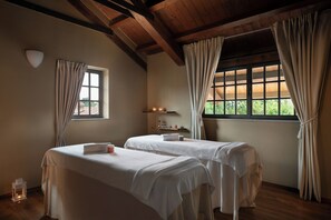 Una habitación con dos camas, una ventana con cortinas, un estante con velas y un pequeño farol.