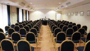 Un salón de conferencias con filas de sillas, un atril y una pizarra.