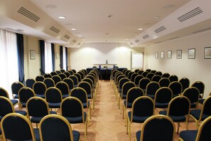 Un salón de conferencias con filas de sillas, un atril y una pizarra.