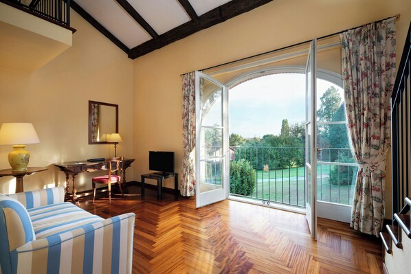 A room with a wooden floor, a striped sofa, a desk with a chair, a television, and a large sliding glass door leading to a garden. - Sina Villa Matilde (Romano Canavese)