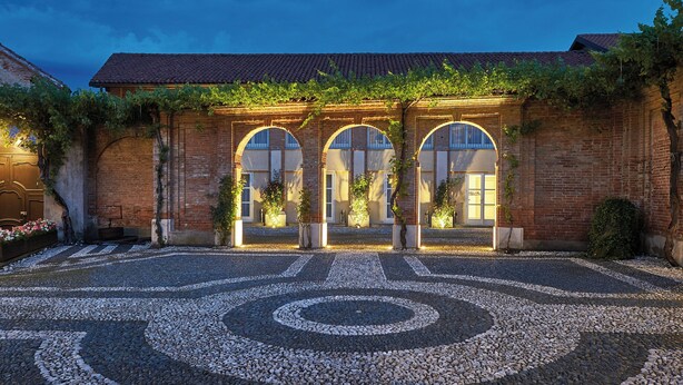 Un edificio con ventanas de arco, un patio de piedra con diseño y fachada de ladrillo.