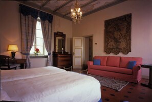 A bedroom with a large bed, a red sofa, a chandelier, a large painting, and a wooden dresser. - Sina Villa Matilde (Romano Canavese)