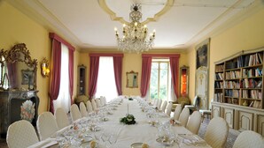 A formal dining room with a long table set for a meal, chandeliers, and a bookshelf. - Sina Villa Matilde (Romano Canavese)