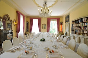 A formal dining room with a long table set for a meal, chandeliers, and a bookshelf. - Sina Villa Matilde (Romano Canavese)