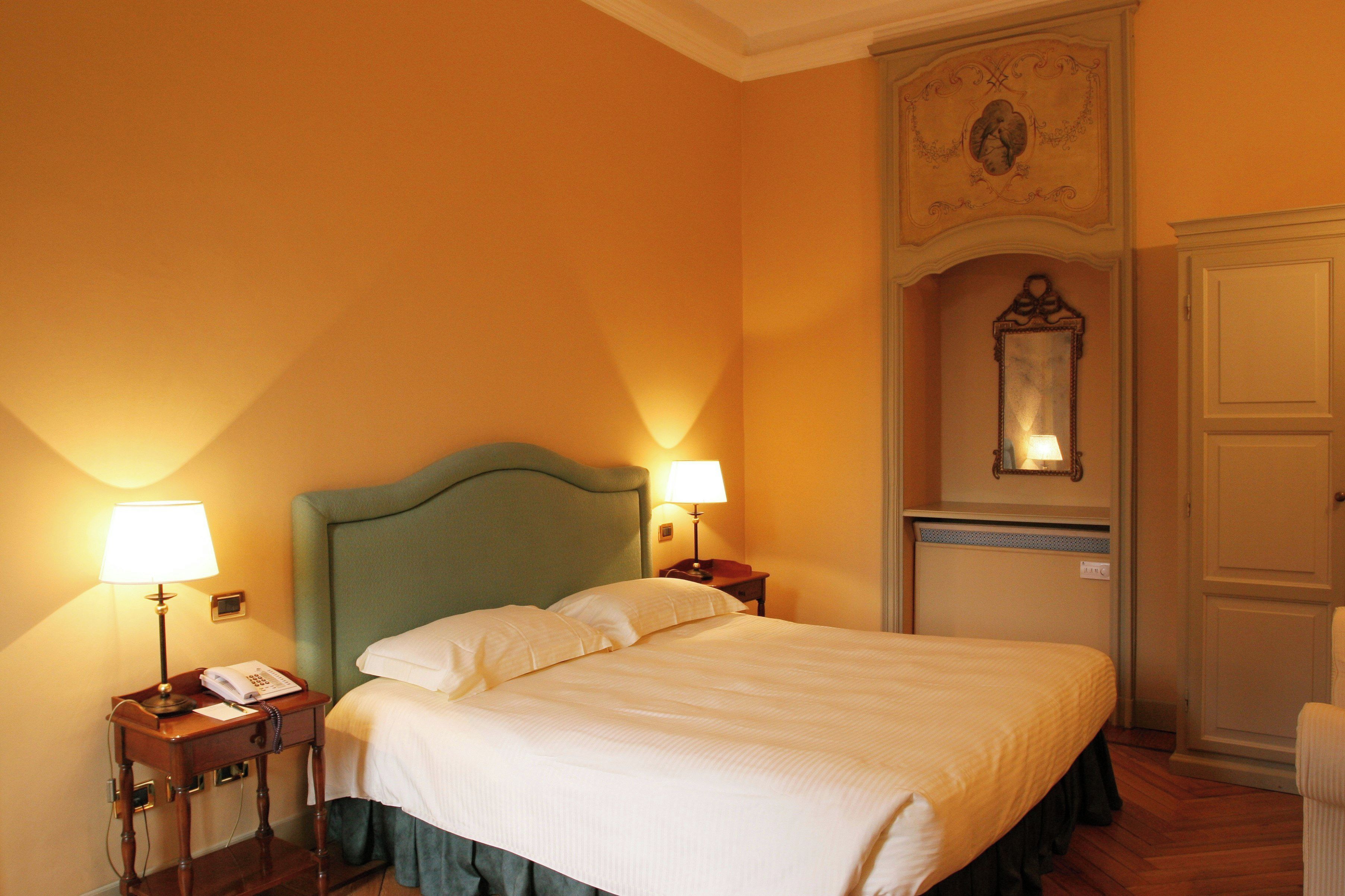 Ein Hotelzimmer mit einem Bett, zwei Nachttischlampen, einem Telefon, einem Spiegel und einer Tür.