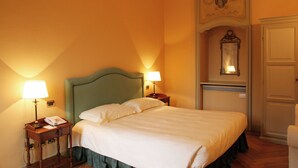 Una habitación de hotel con cama, dos lámparas de noche, teléfono, espejo y puerta.