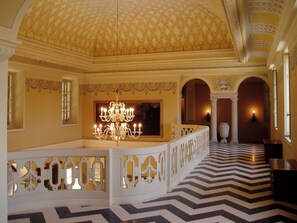 Una sala imponente con un gran candelabro, techo ornamentado y un suelo con diseño.