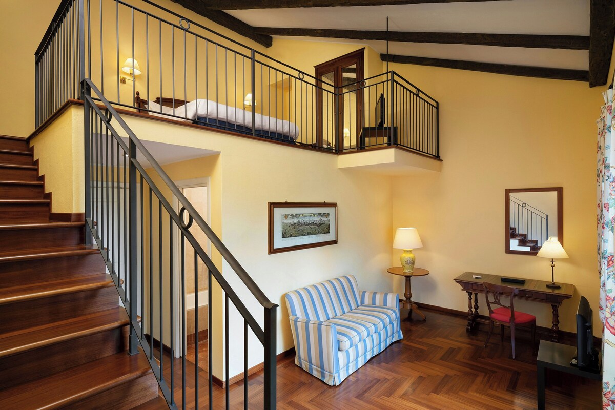 Una escalera con detalles de madera, un sofá a rayas, un escritorio con una silla y un cuadro en la pared.