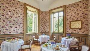 A dining area with floral wallpaper, multiple tables, chairs, and large windows. - Sina Villa Matilde (Romano Canavese)