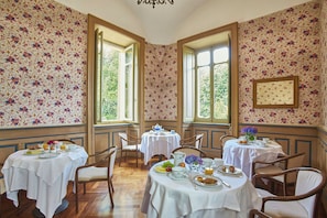 A dining area with floral wallpaper, multiple tables, chairs, and large windows. - Sina Villa Matilde (Romano Canavese)