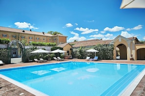 Una piscina con sillas de descanso y sombrillas, rodeada de edificios con tejados de tejas.