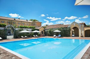 Una piscina con sillas de descanso y sombrillas, rodeada de edificios con tejados de tejas.
