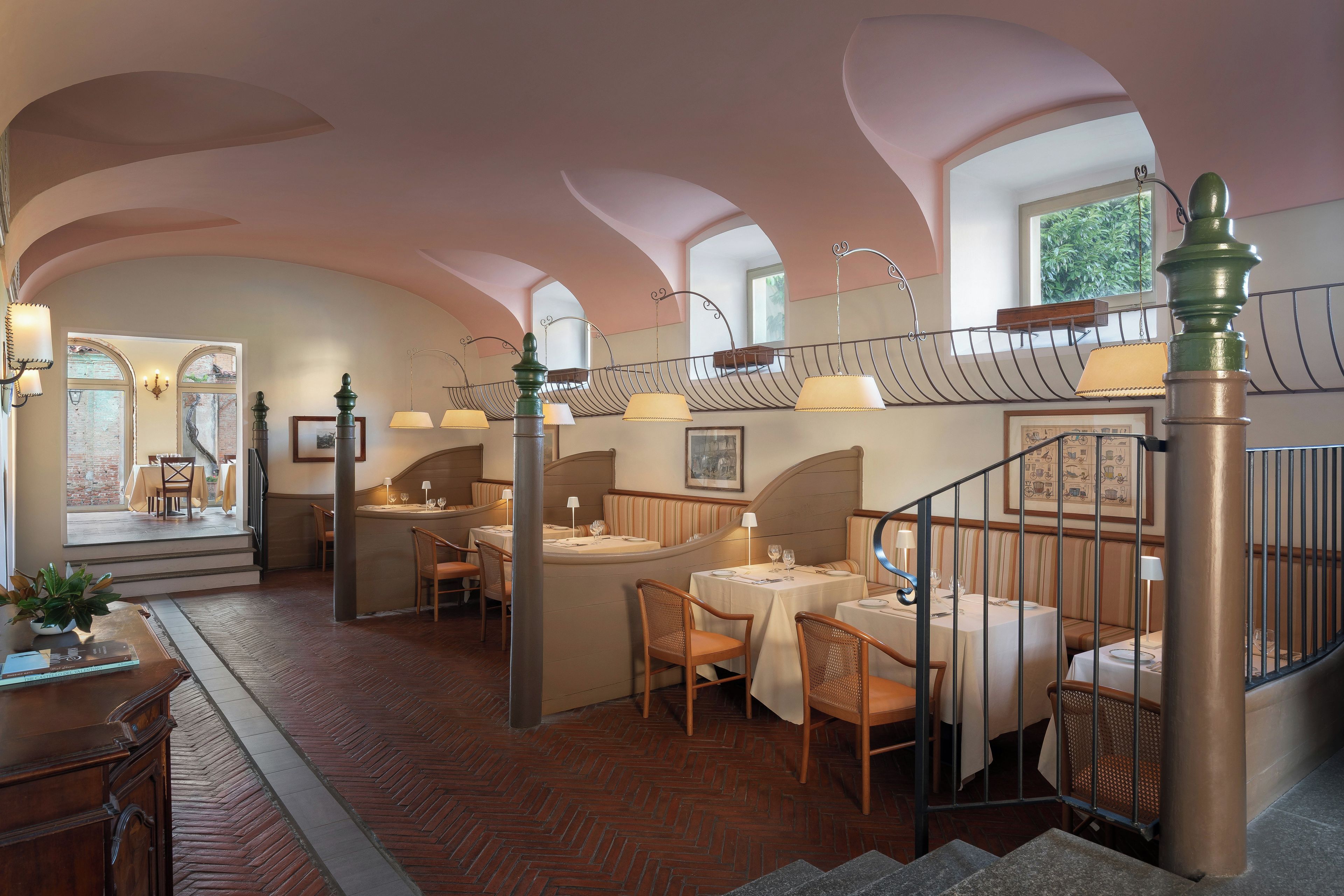 A restaurant with a brick floor, arched ceilings, and a staircase with a metal railing.