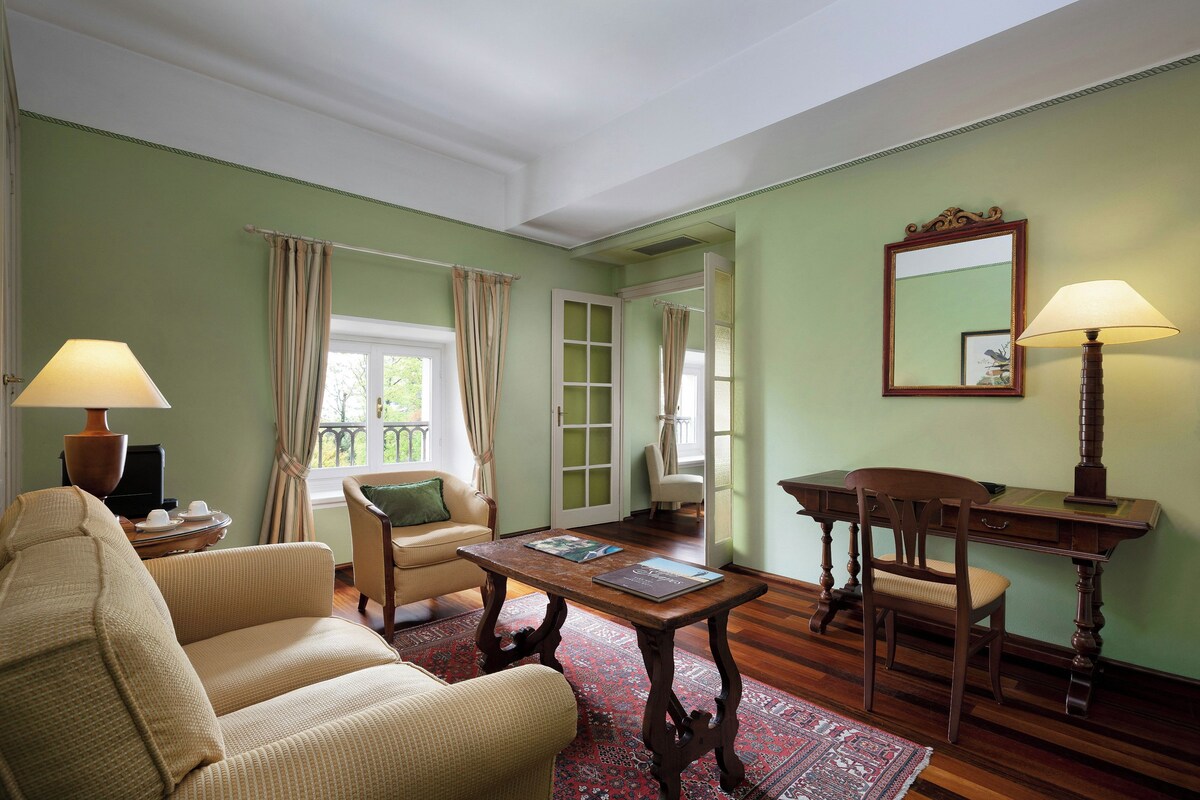 Una habitación con un sofá, una mesa de madera con una lámpara, una silla, un escritorio y un espejo en la pared.