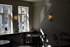 Un comedor con mesas y sillas, ventanas amplias con persianas y luces fijadas a la pared.