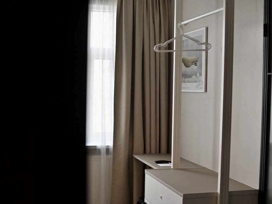 A hotel room with a large window, a mirror, a white dresser, and a hanging coat rack.