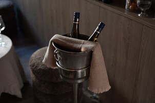 Un secchio di metallo con due bottiglie di vino, coperte da un panno, appoggiato su uno sgabello.