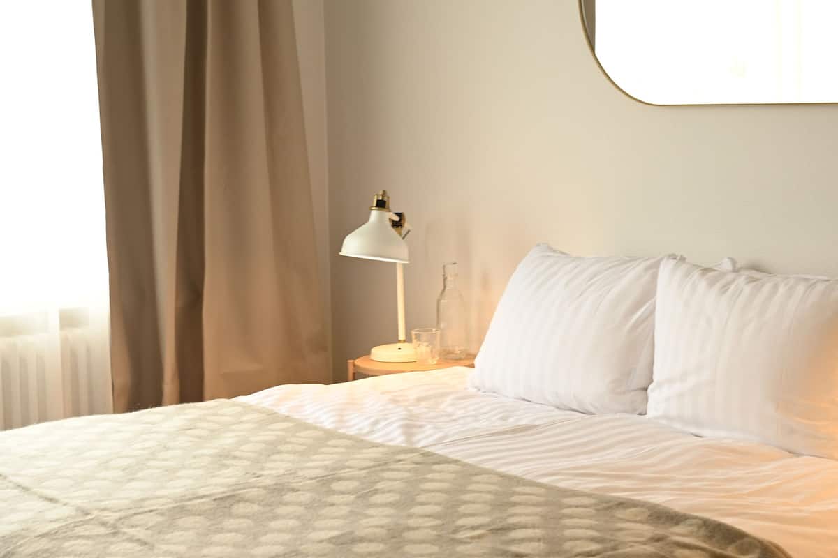 A neatly made bed with a patterned blanket, a bedside lamp, and a mirror on the wall.