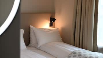 Ein Hotelzimmer mit einem ordentlich bezogenem Bett, einer Wandleuchte und einem Fenster mit Vorhängen.