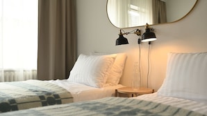 Habitación de hotel con dos camas, una mesita de madera redonda, un espejo y dos lámparas de escritorio negras.