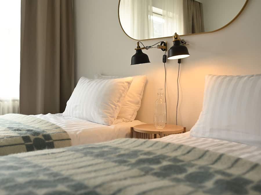 Et hotelværelse med to senge, et rundt træsidebord, et spejl og to sorte skrivebordslamper.
