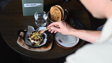 A person eating a dish with cranberries and nuts, a glass of water, and a bread roll on a wooden table.