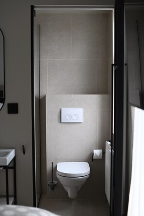 Un baño pequeño y moderno con inodoro, bidé y dispensador de toallas.