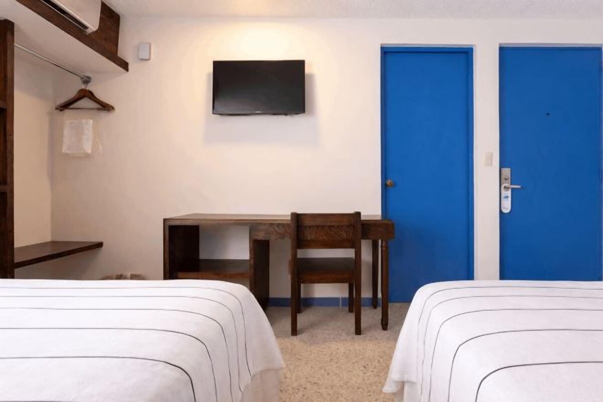 Een kamer met twee bedden, een bureau, een stoel, een televisie en twee blauwe deuren.