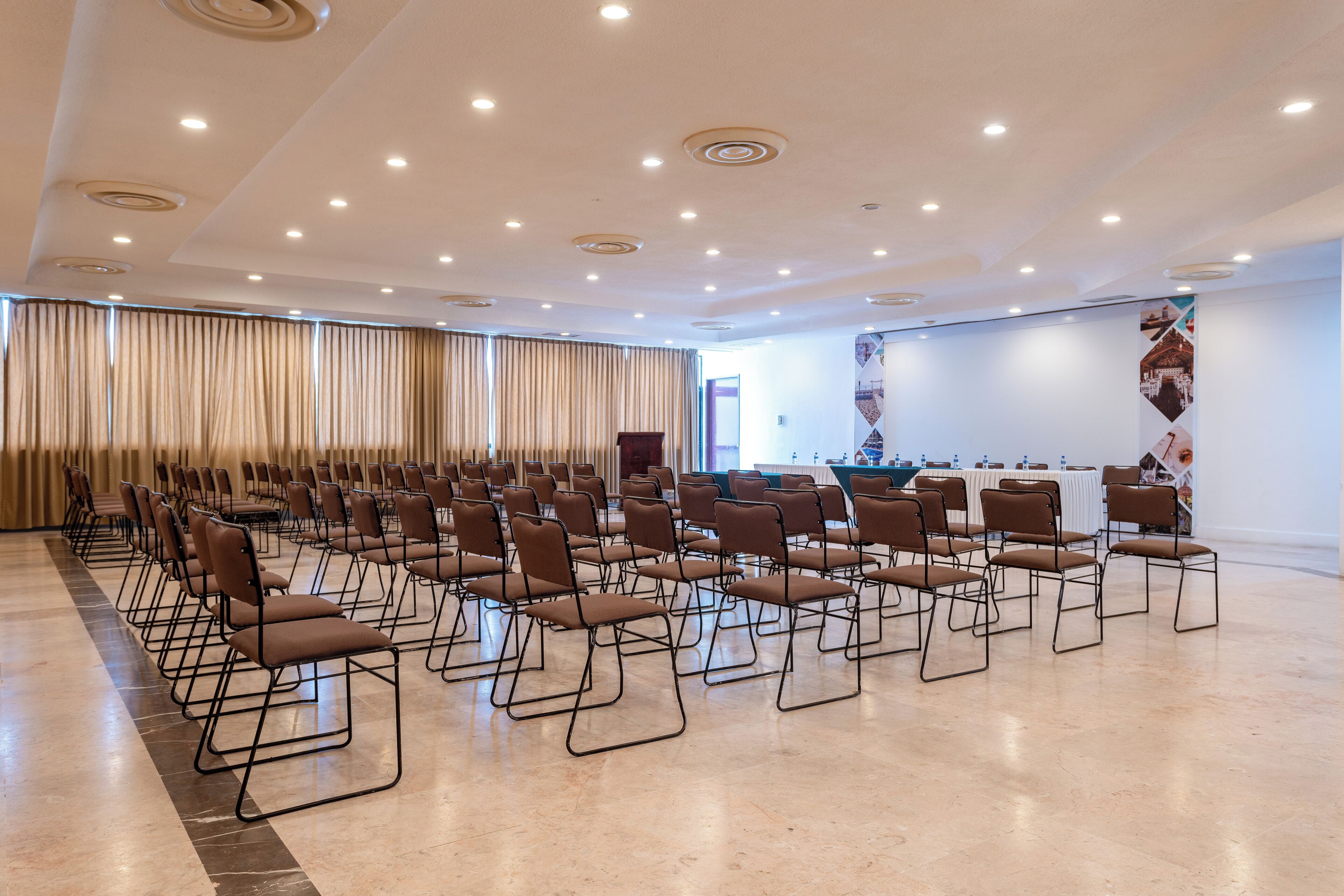 Une salle de conférence avec des rangées de chaises, une scène et une grande bannière accrochée au mur.